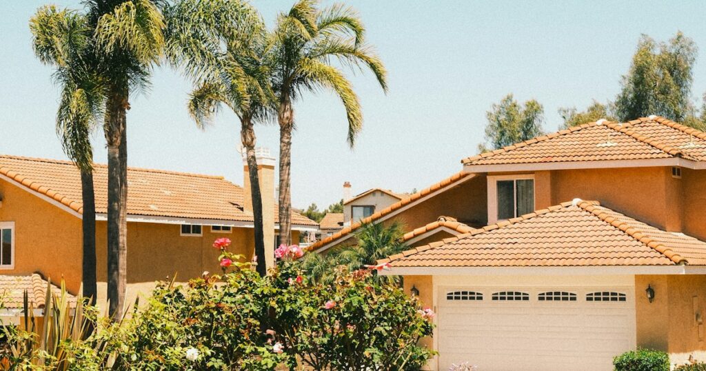 Suburban homes with tile roofs, palm trees and rose bushes under a clear sky