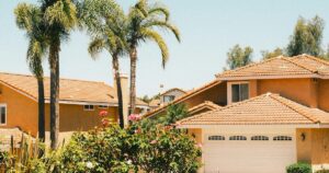 Suburban homes with tile roofs, palm trees and rose bushes under a clear sky