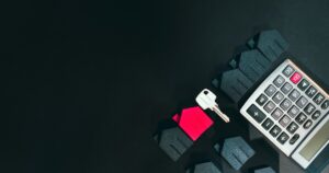 A house key, a red model house and a calculator on a dark surface